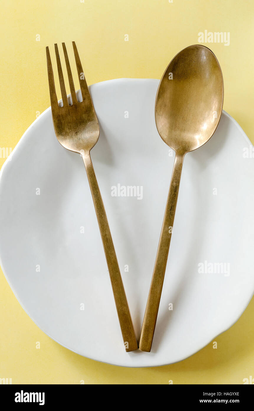 brass spoon and fork on white plate on yellow background Stock Photo Alamy