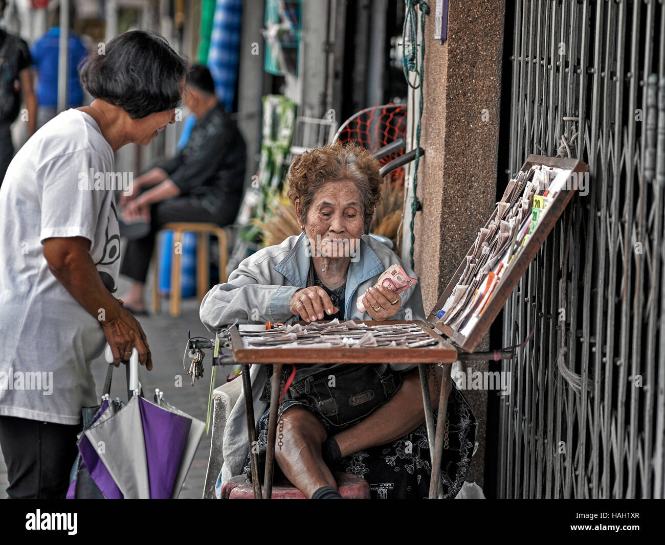 Thailand lottery. Elderly female lottery vendor with customer. Thailand S. E. Asia Stock Photo