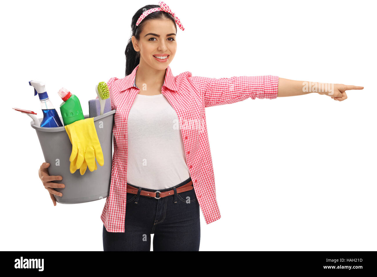 Happy woman holding a bucket filled with cleaning products and pointing right isolated on white background Stock Photo