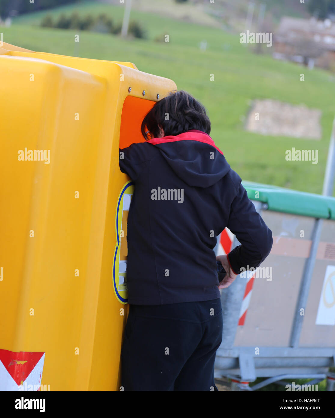 poor young boy looks into the yellow garbage can in search of something Stock Photo