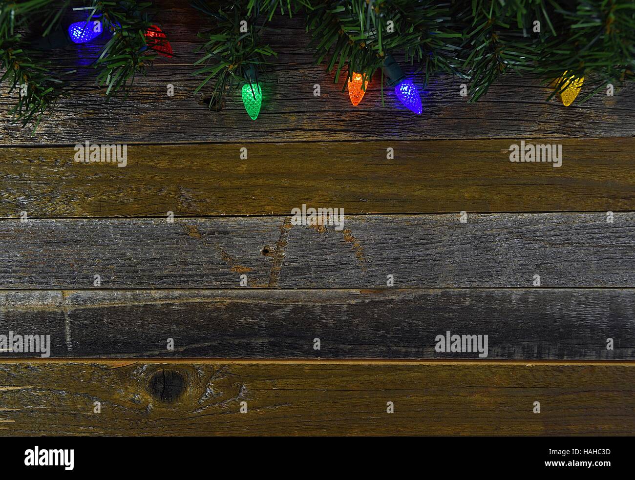 glowing Christmas lights and pine border on rustic barn wood Stock Photo