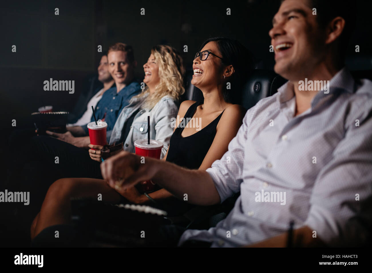 Young people sitting in multiplex movie theater watching movie and smiling. Stock Photo