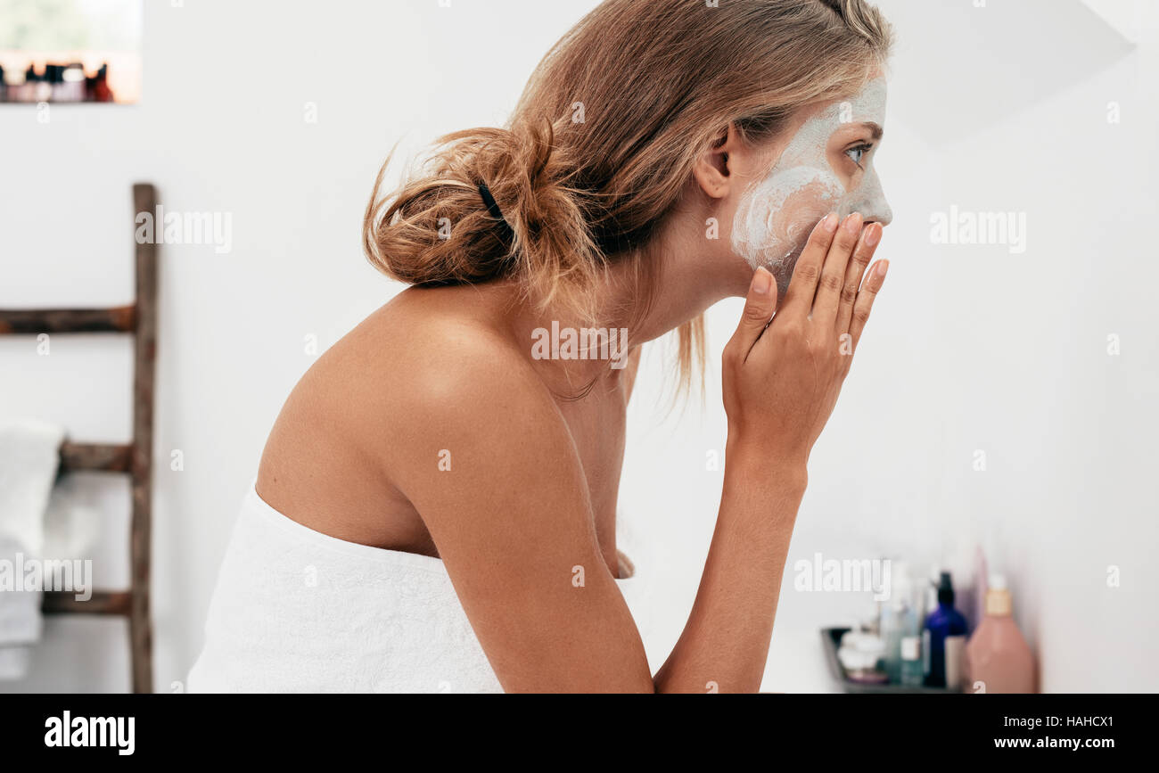 Side view shot of young woman applying facial cosmetic mask in bathroom.  Female taking care of her face skin. Stock Photo