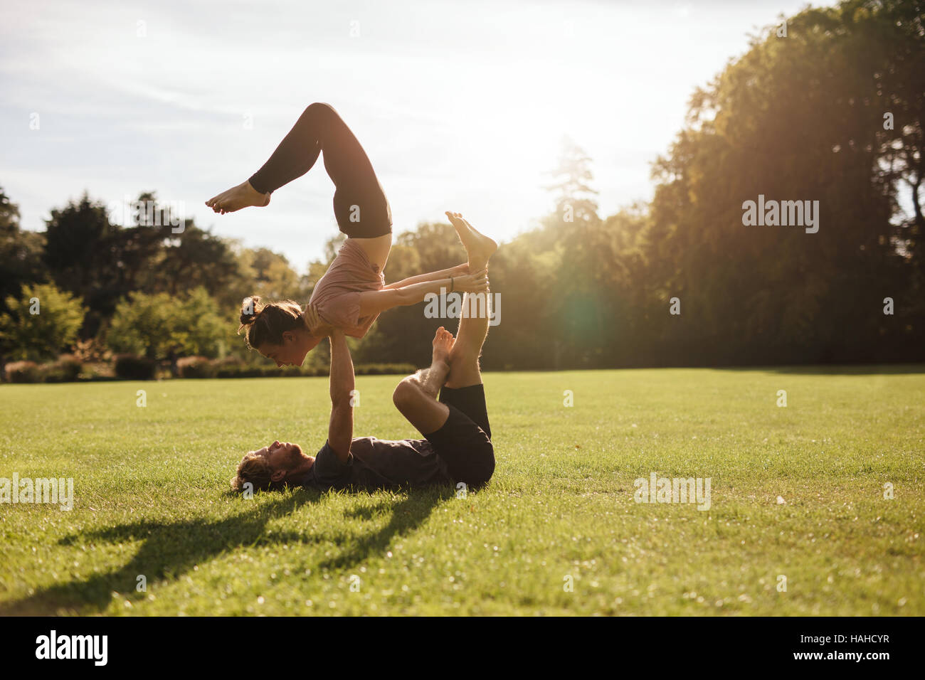 Strong young couple doing acroyoga workout. Man and woman in park practising pair yoga in morning. Stock Photo