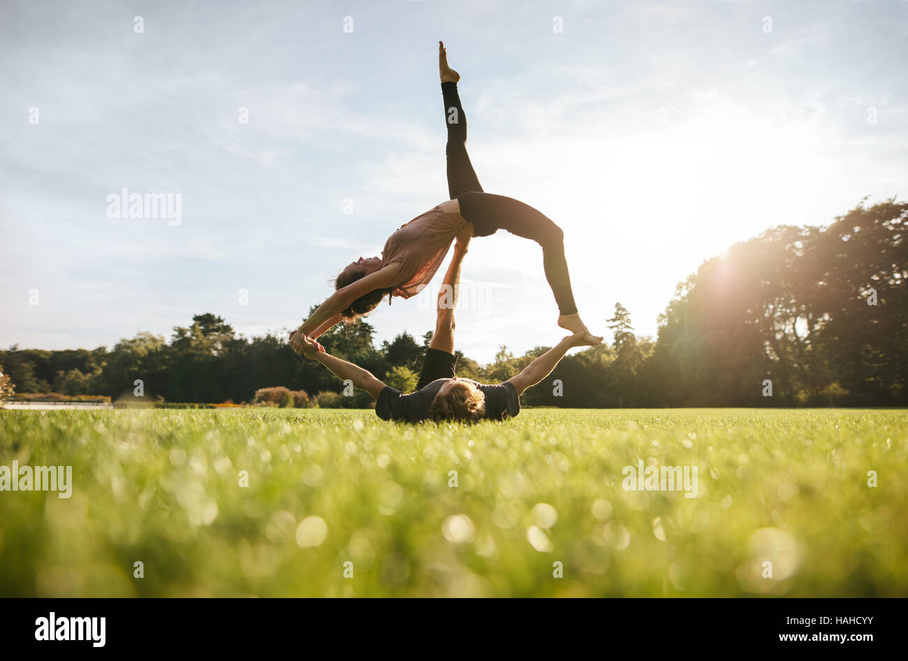 Shot of young couple doing acrobatic yoga on lawn. Young man lifting and balancing woman at the park. Stock Photo