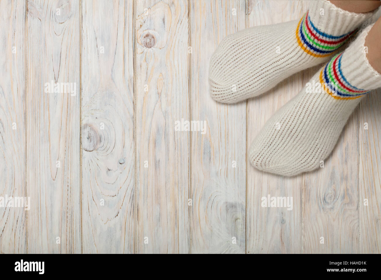 Female feet in knitted white socks on white wooden background Stock