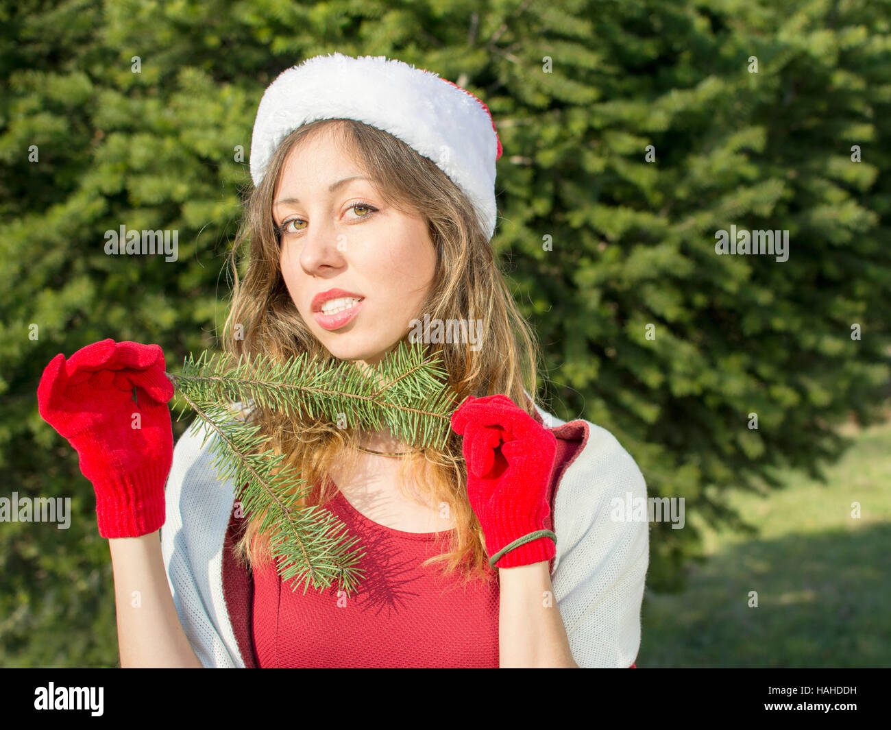 Beautiful Santa Claus girl with with fir tree branch in front big fir tree Stock Photo