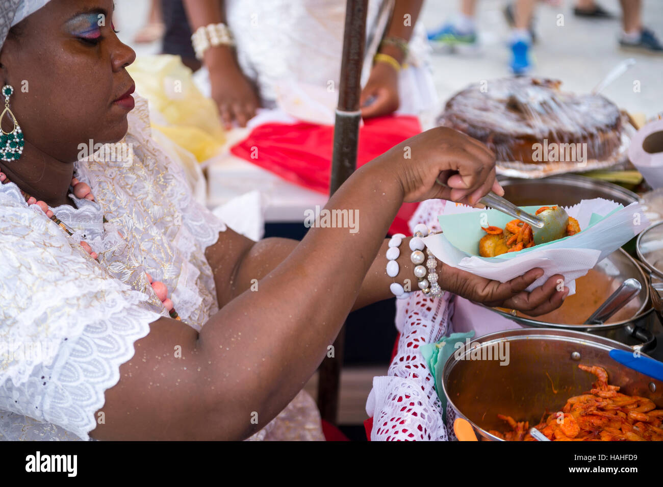 SALVADOR, BRAZIL - FEBRUARY 02, 2016: Brazilian Baiana woman assembles a plate of traditional acaraje fritters from a stall. Stock Photo