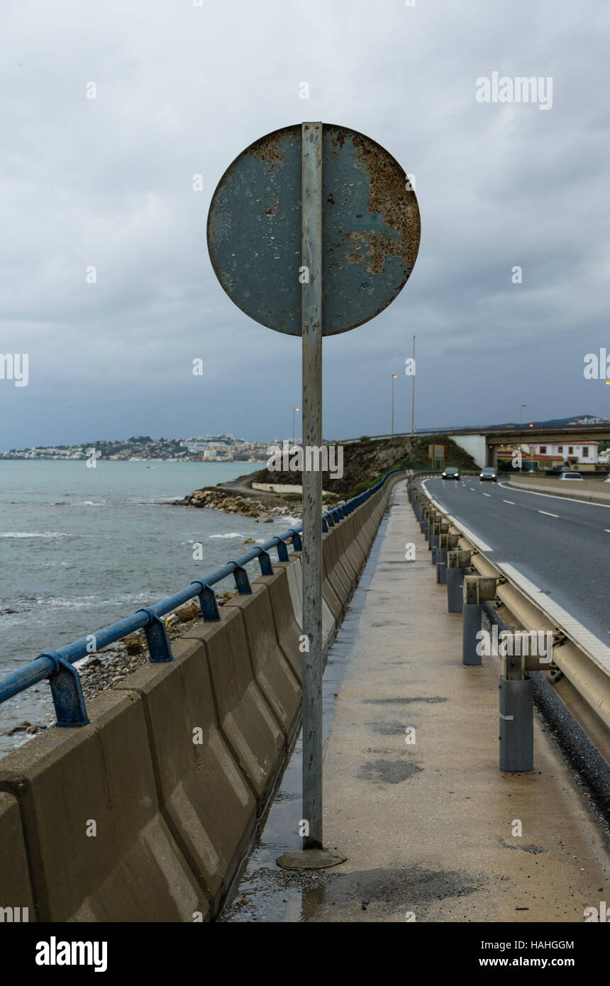 Roadside sign from behind with road next to sea during clouded day. Spain. Stock Photo