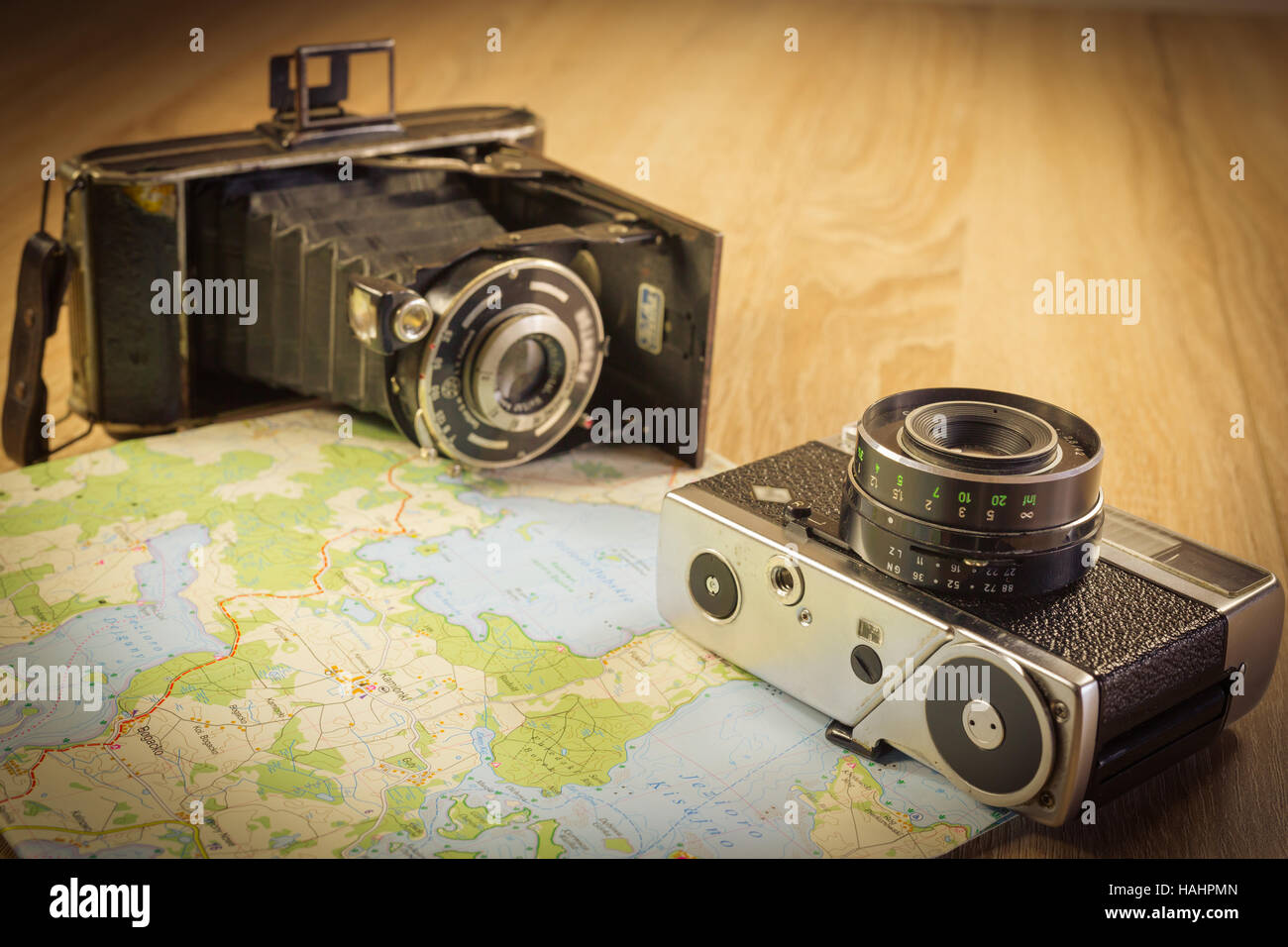 Old photo camera, with slightly newer one on a map. Photo camera prepared to be taken on a trip. Stock Photo