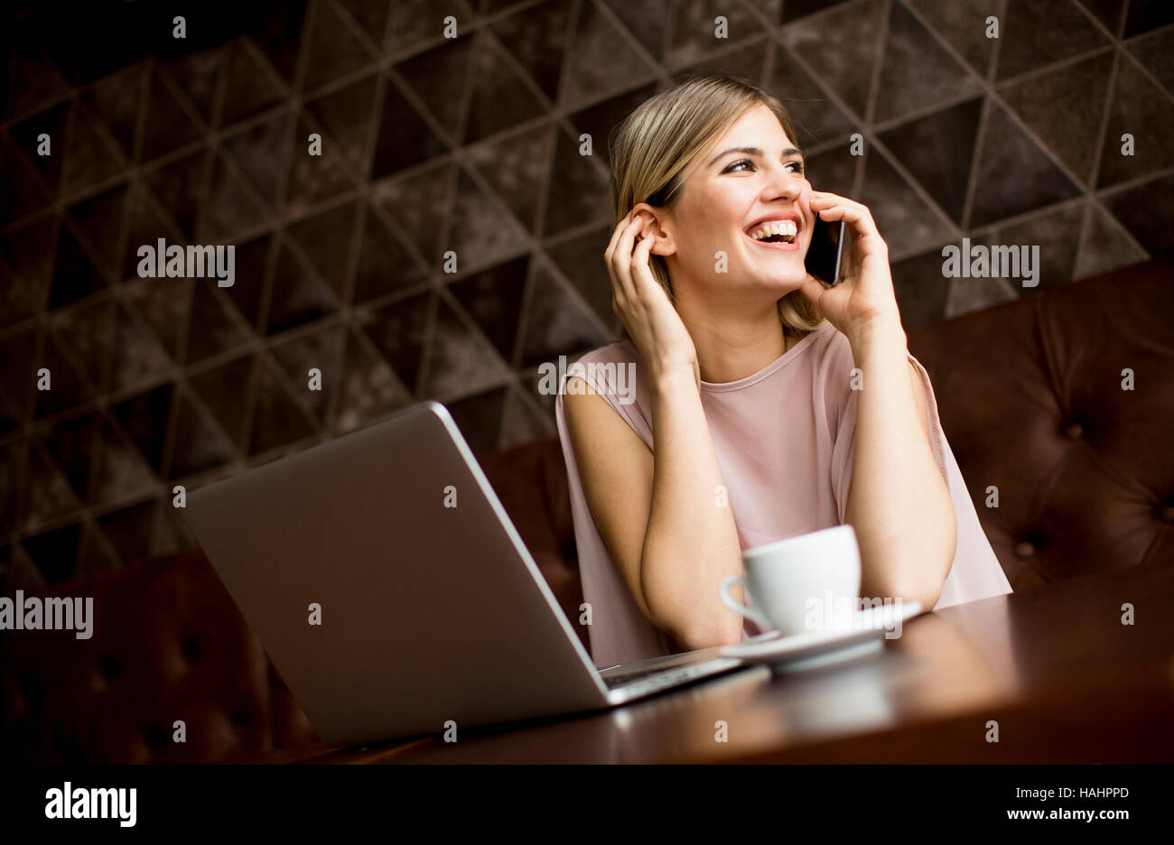 Freelance young woman sitting in the cafeteria with laptop and using  mobile phone Stock Photo