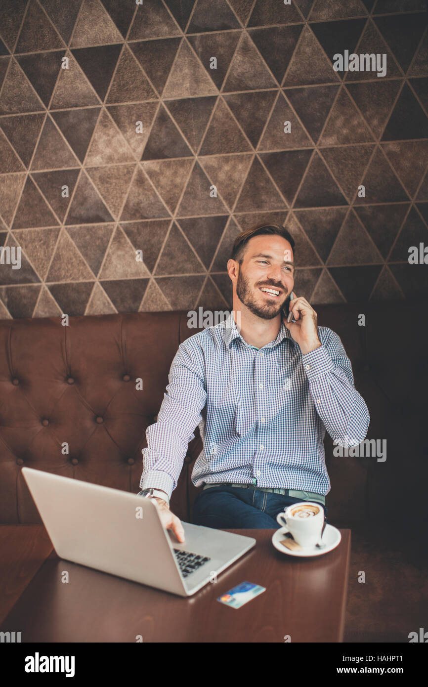 Young man sitting in cafe and using laptop and mobile phone Stock Photo