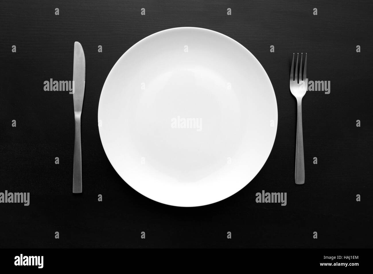 empty white plate with fork and knife on dark wooden table Stock Photo