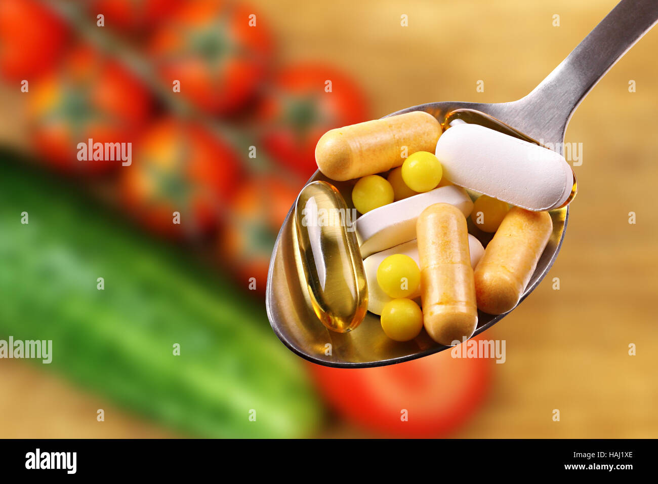 spoon with tablets and capsules on vegetables background Stock Photo