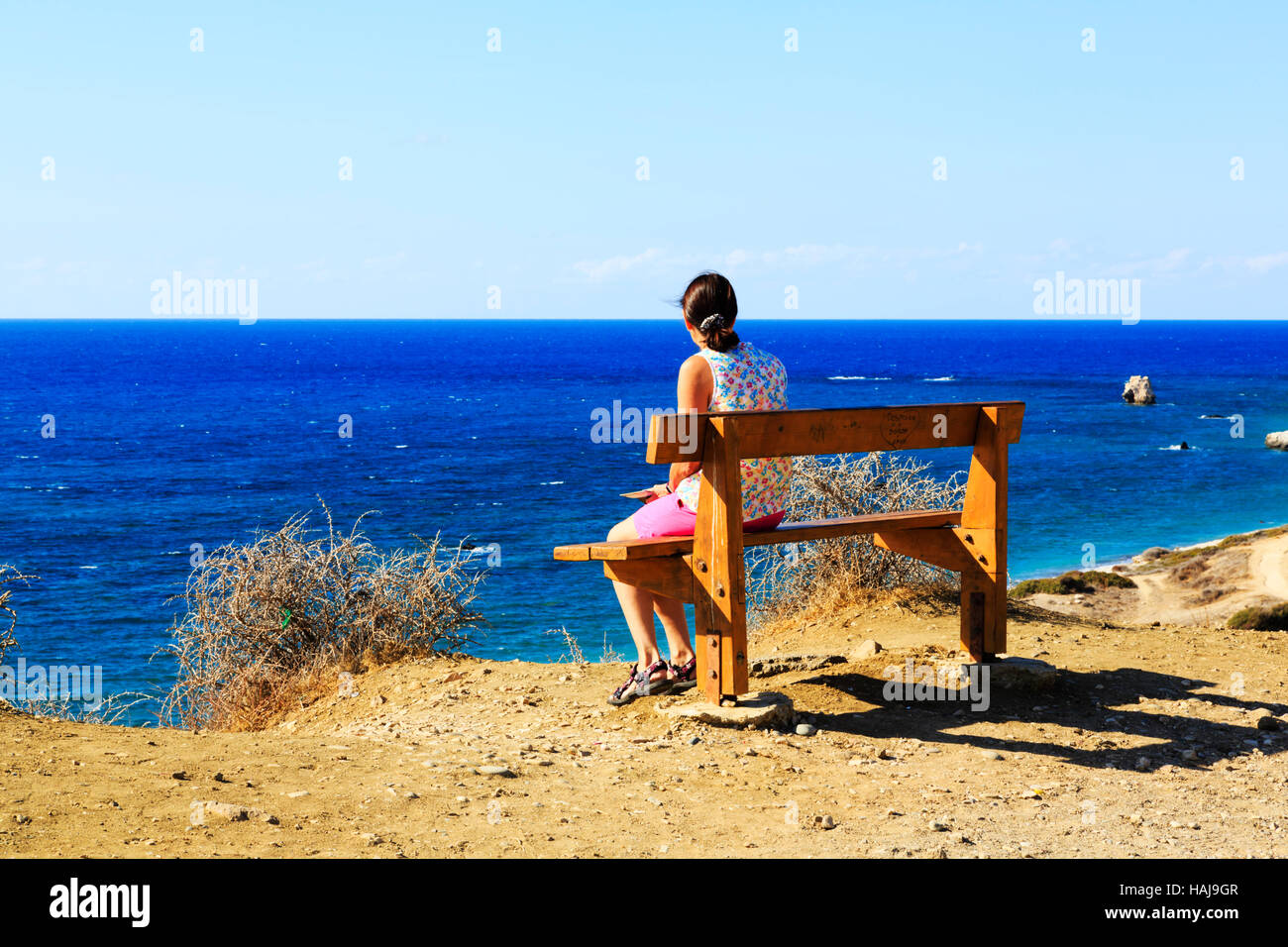 Women sitting on a bench on a cliff, looking out over the blue sea ...