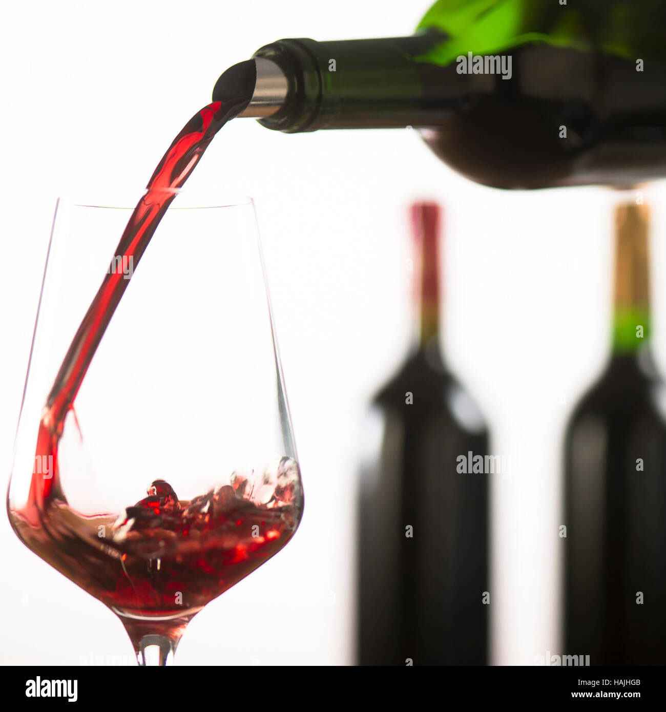 Pouring red wine into wineglass from green bottle, white background Stock Photo