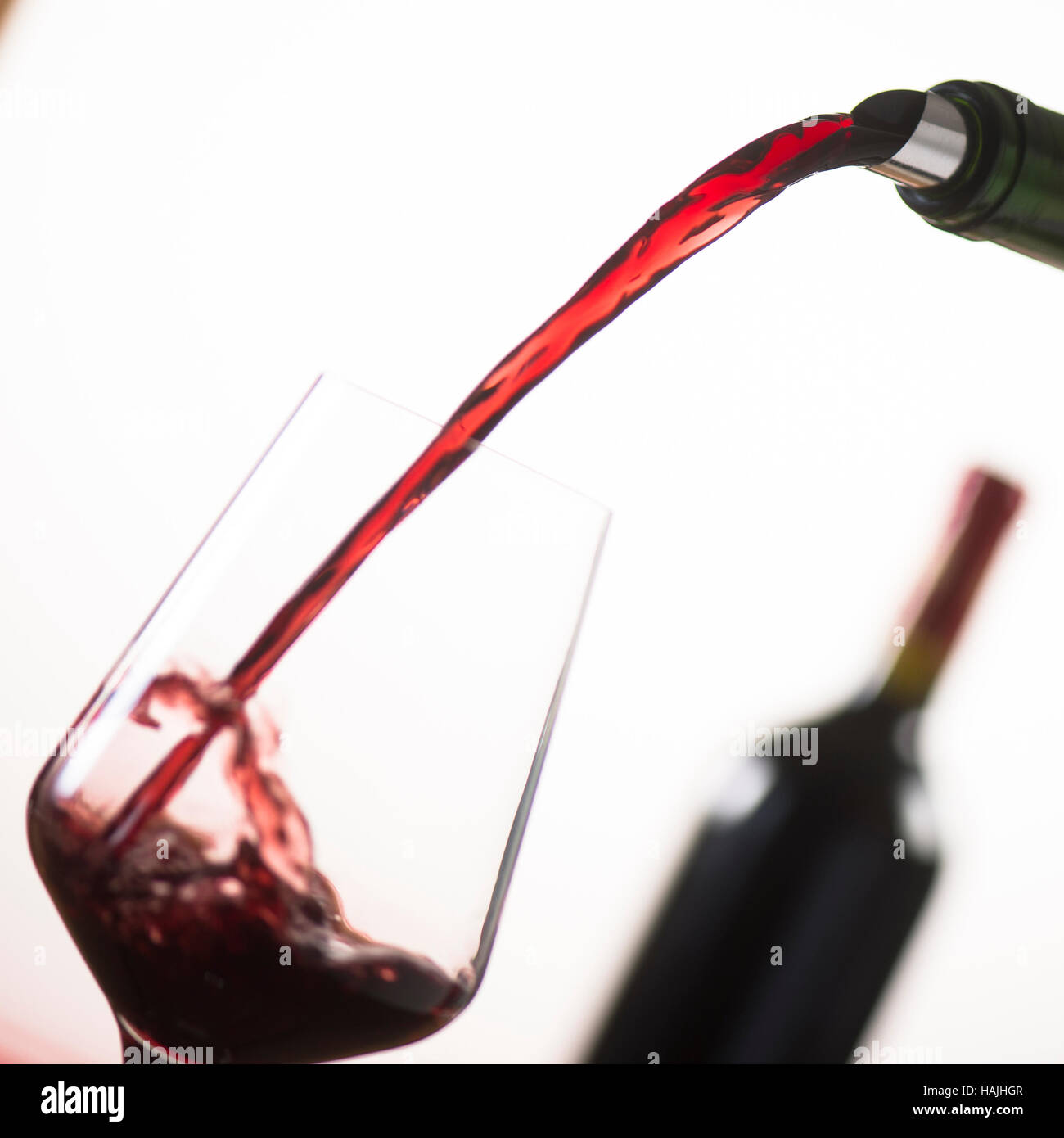 Pouring red wine into wineglass from green bottle, white background Stock Photo