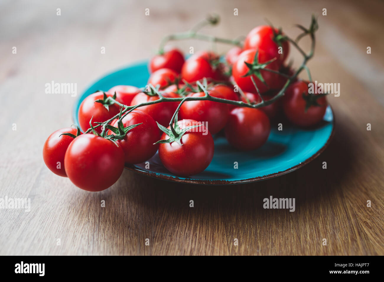 Cherry tomatoes on the vine. Blue plate of cherry tomatoes on wooden table. Stock Photo