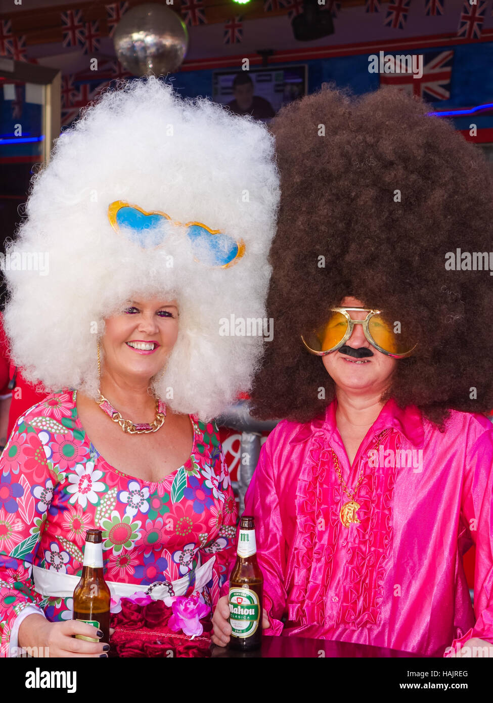 British fancy dress street party in Benidorm, Spain. Couple with massive giant afro wigs sixties sunglasses. Stock Photo