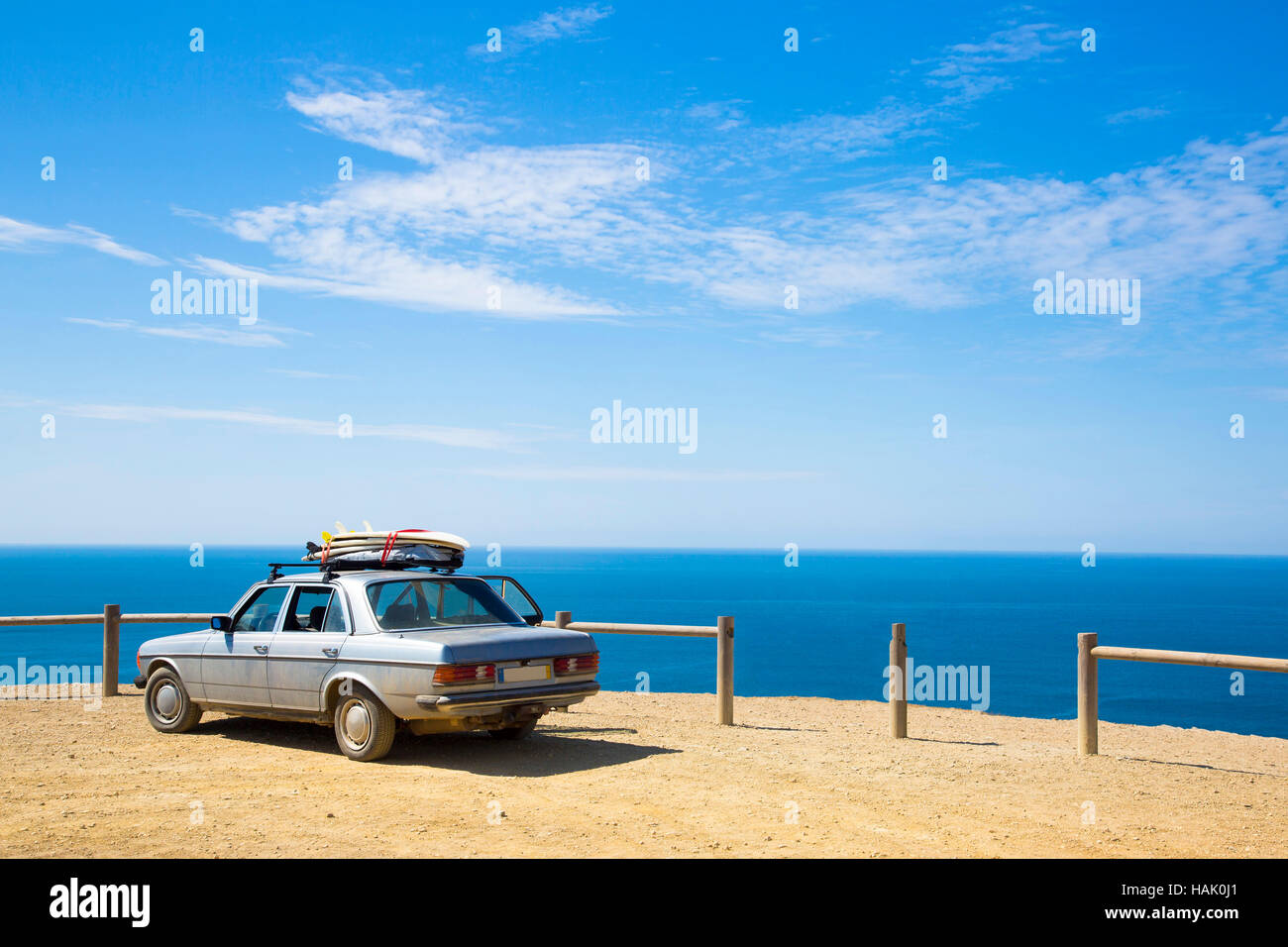 old retro car with surfboards on the roof and ocean in background Stock Photo