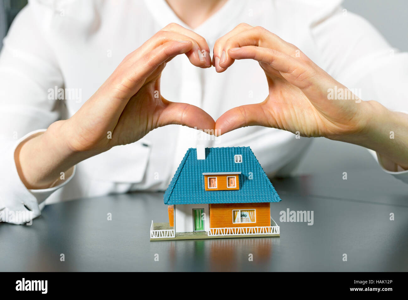 charity, real estate and family home concept - human hand in heart shape above small plastic house Stock Photo