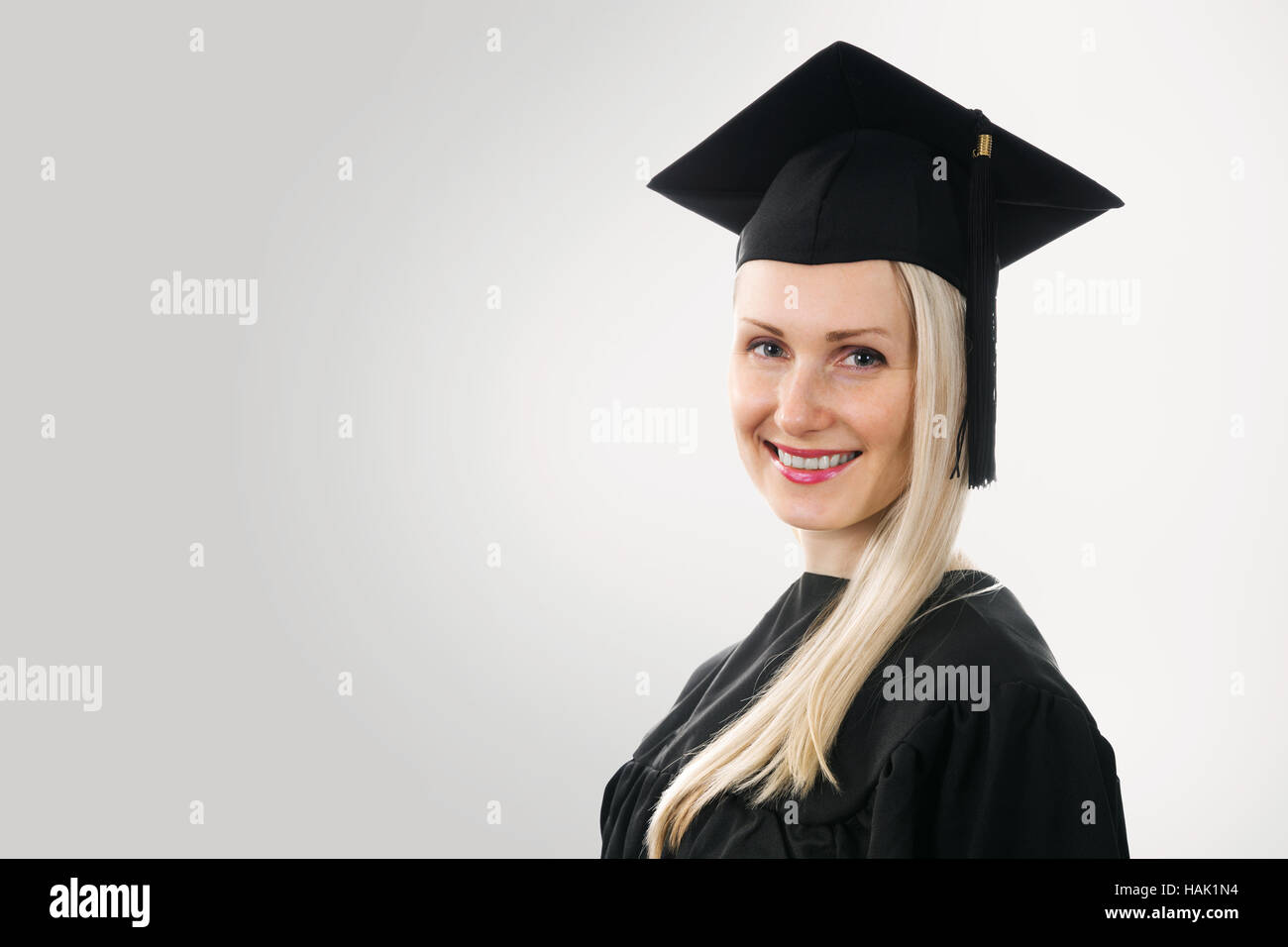 university graduate wearing cap and gown on gray background with copyspace Stock Photo