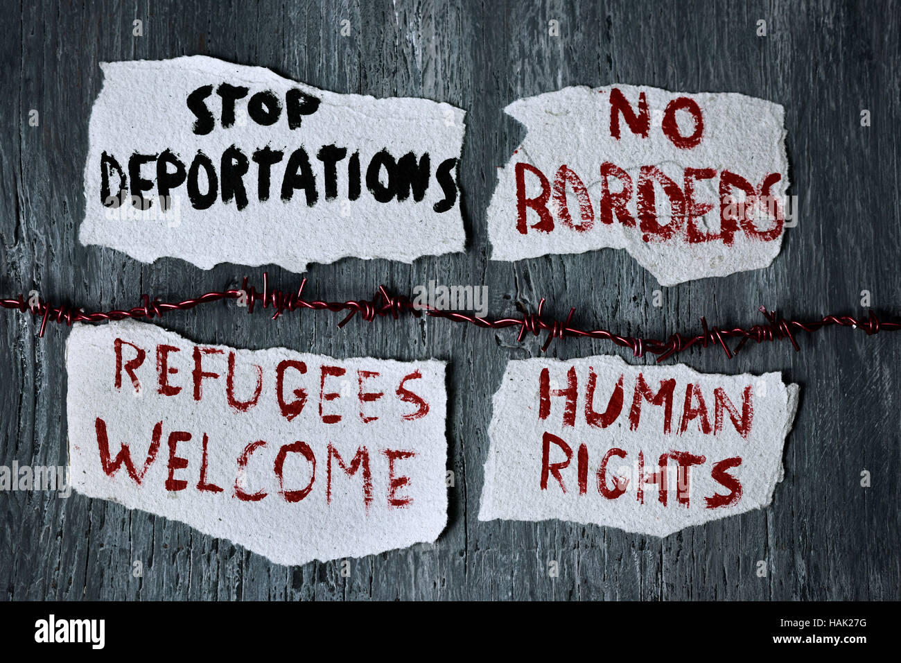 high-angle shot of a barbed wire and some pieces of paper with different messages, such as stop deportations, no borders, refugees welcome and human r Stock Photo