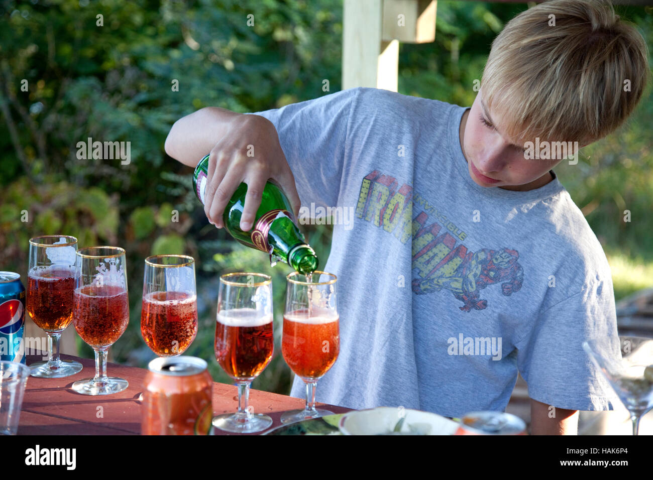 Acting bartender boy age 13 filling stemmed glasses with juice for a family toast. Clitherall Minnesota MN USA Stock Photo