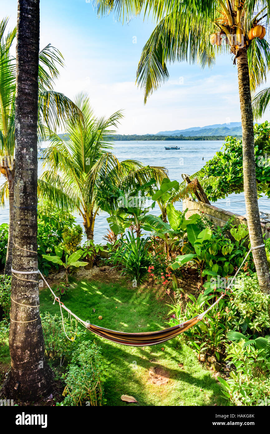 Riverside view with hammock hanging between coconut palms in Caribbean town of Livingston, Guatemala, Central America Stock Photo
