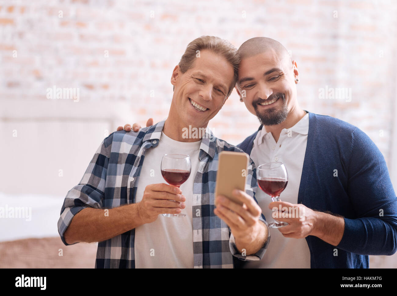 Delighted non-traditional couple drinking wine and taking selfie Stock ...