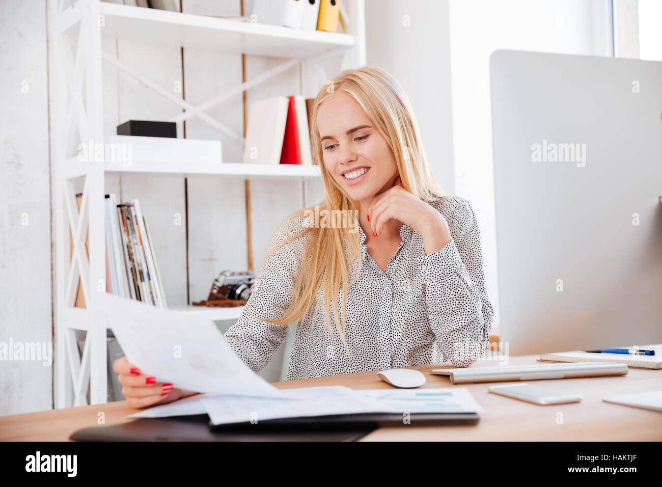 Smiling business woman holding folder while sitting at her workplace ...