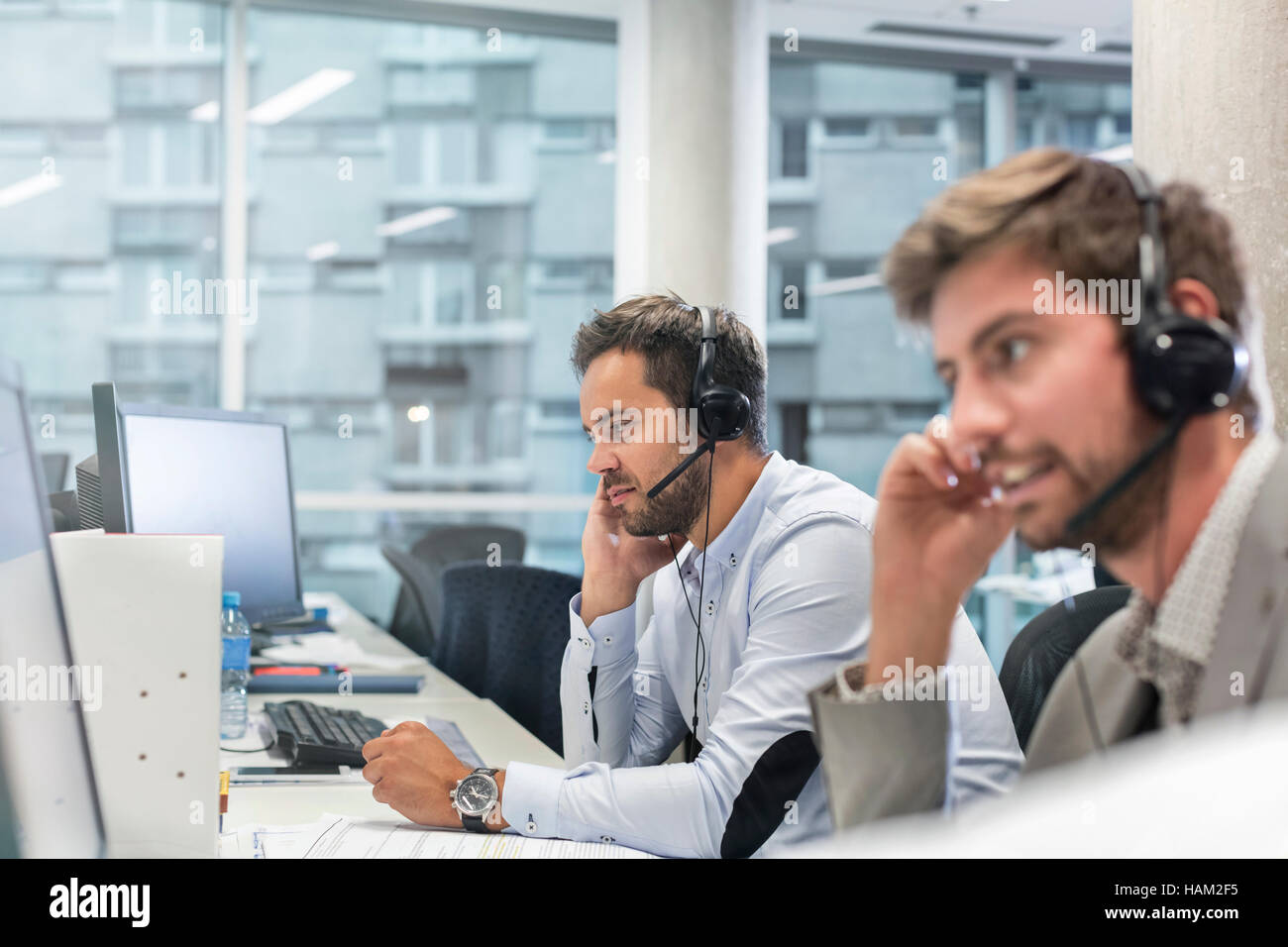 Businessmen with hands-free devices talking on telephone working at computers in office Stock Photo