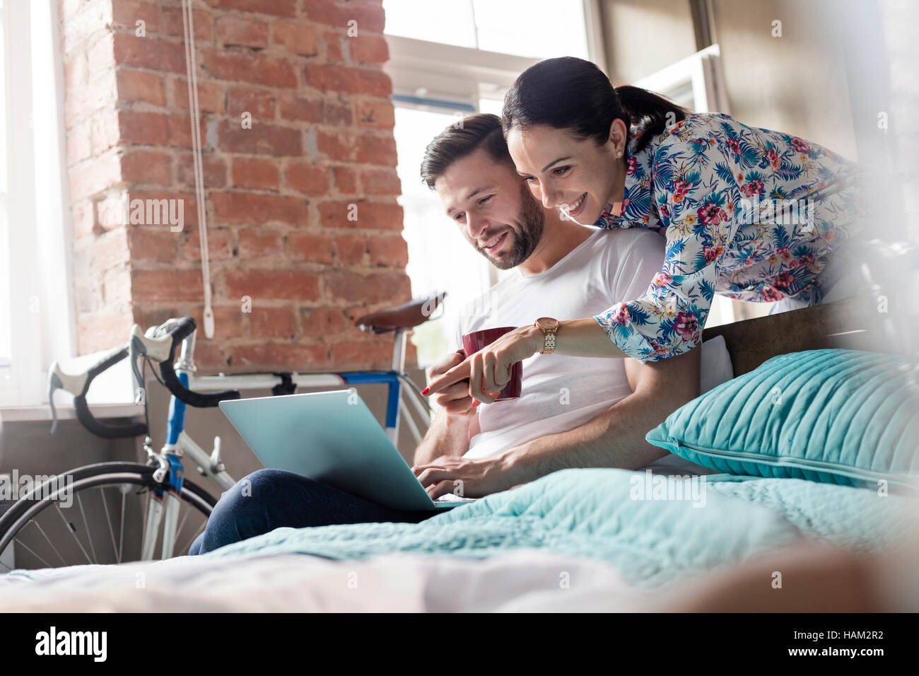 Couple drinking coffee using laptop on bed Stock Photo