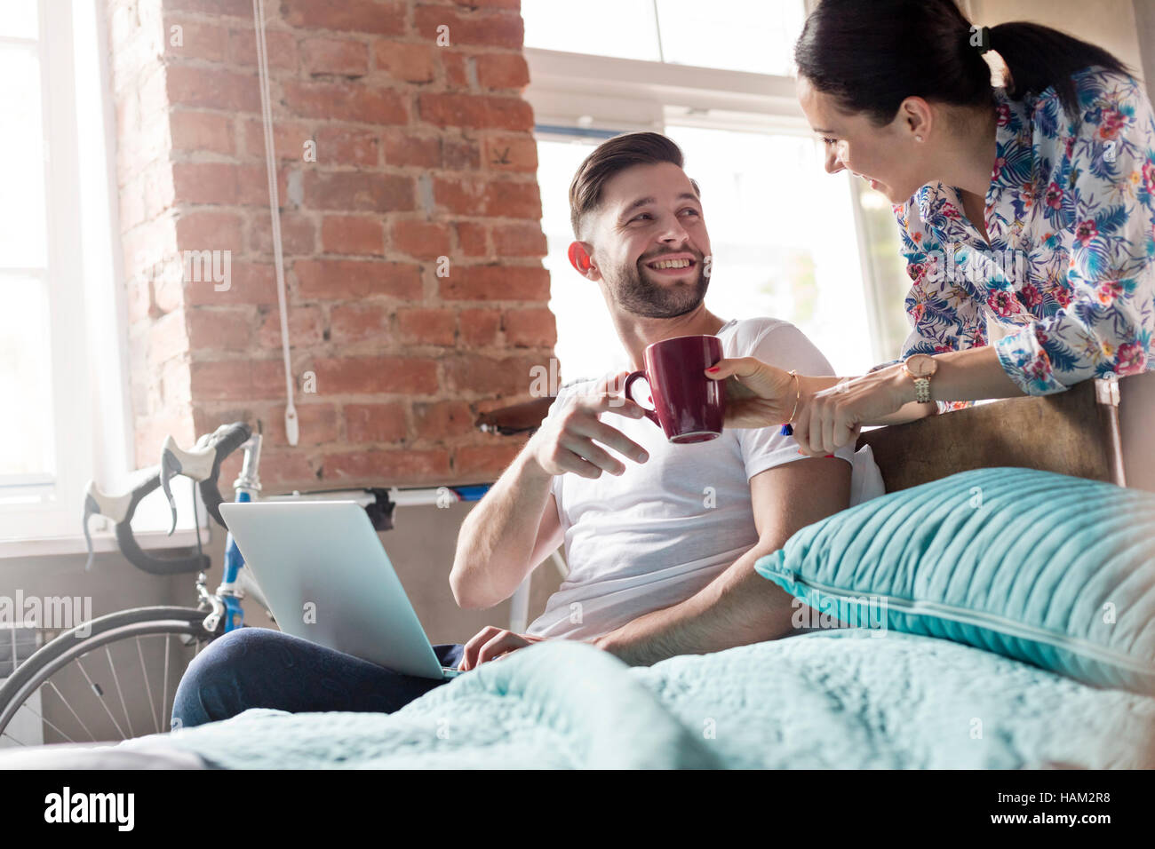 Girlfriend bringing coffee to boyfriend using laptop in bedroom Stock Photo