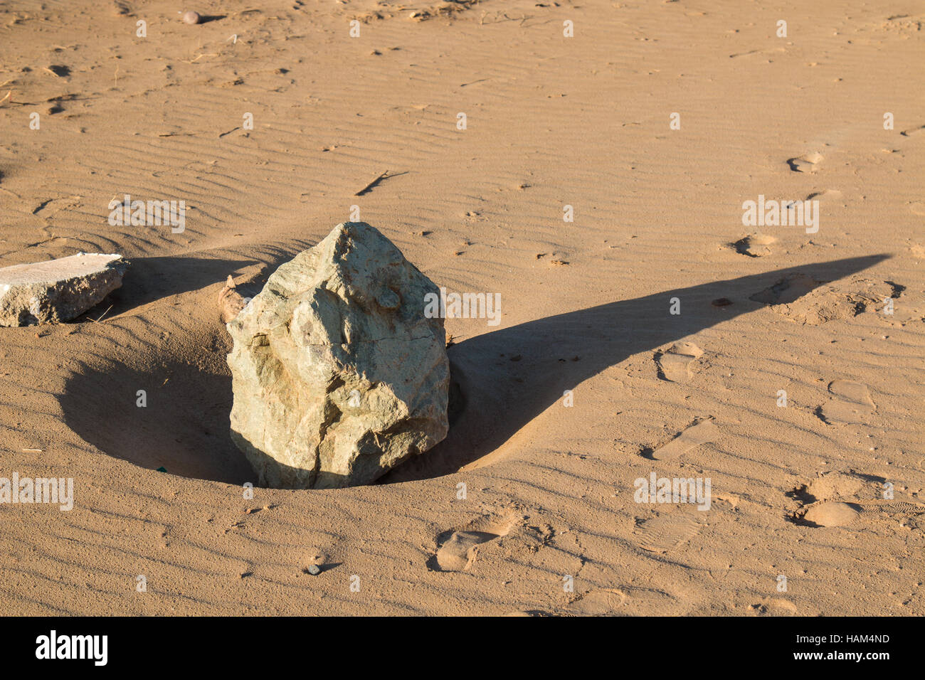 Big Shadowy Rocks Sandy beach in an early morning light. Big stone with a long shadow ...
