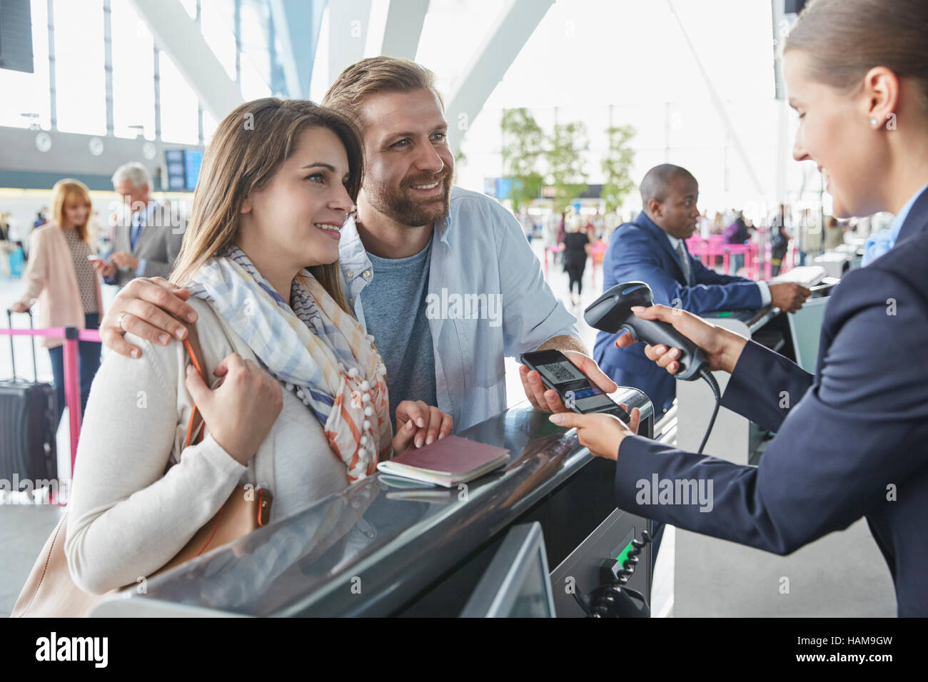 Customer service representative scanning smart phone QR code at airport check-in counter Stock Photo