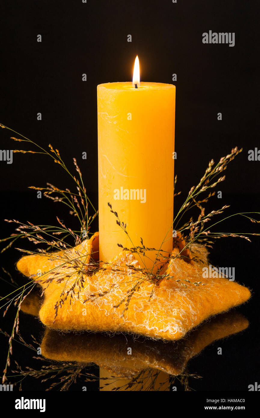 Christmas decoration, golden felted star candle holder, lit candle, dried grasses, black background Stock Photo