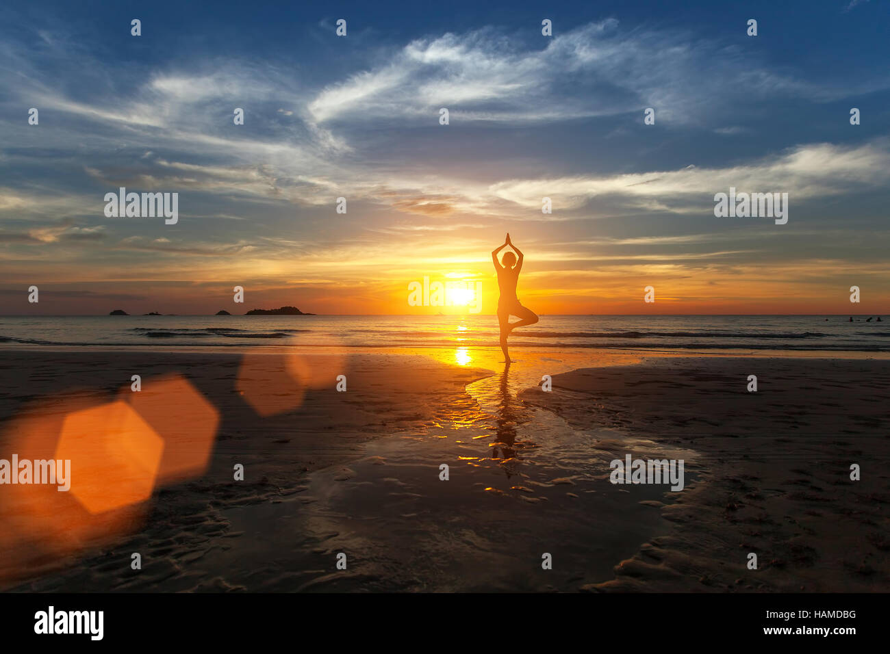 Small silhouette of a woman practicing yoga on sea beach during amazing sunset. Stock Photo