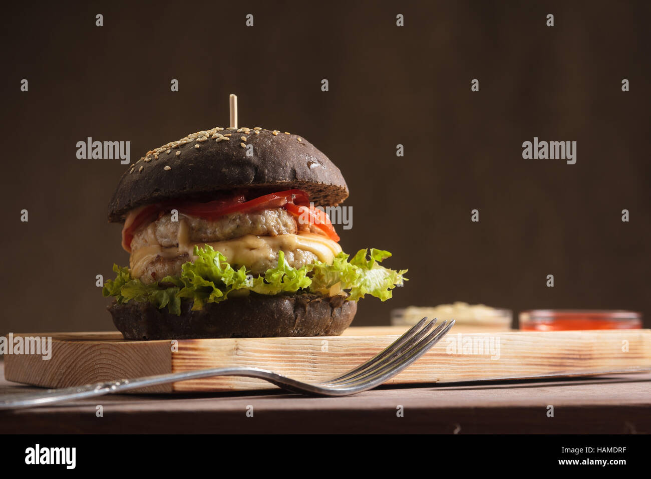 Concept: restaurant menus, healthy eating, homemade, gourmands, gluttony. Trendy burger with chicken in black bun with ingredients on messy vintage wo Stock Photo