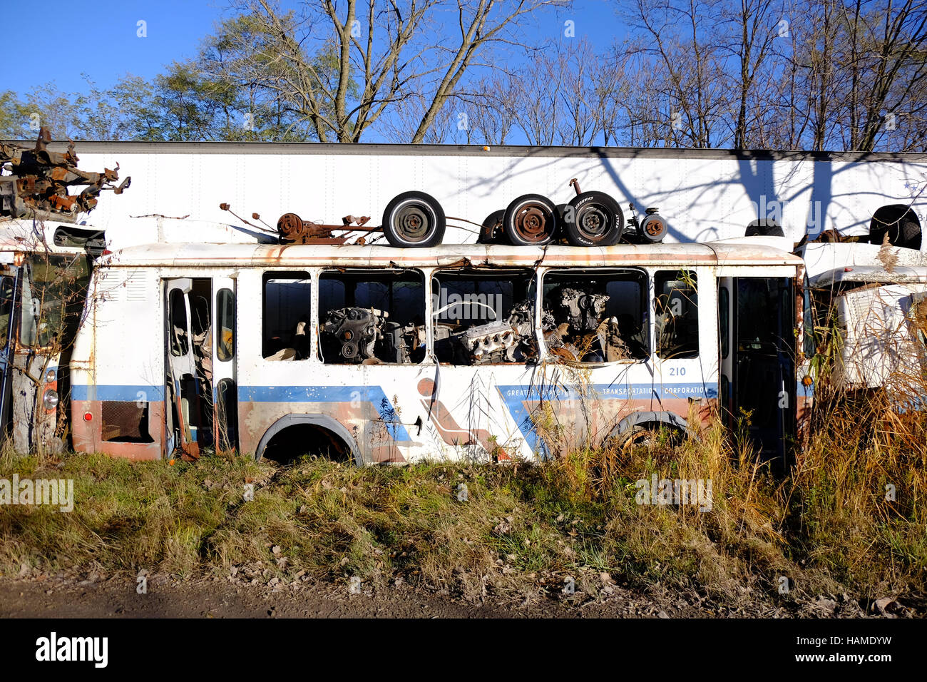 An old city bus sits abandoned in a junkyard with engines stored inside