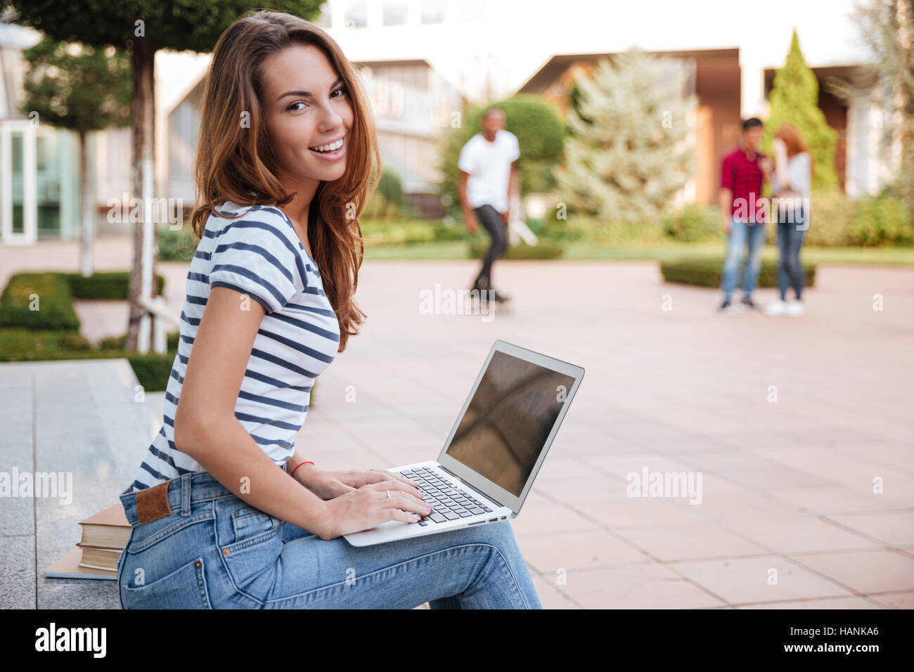 Portrait of smiling cute young woman working with laptop outdoors Stock Photo