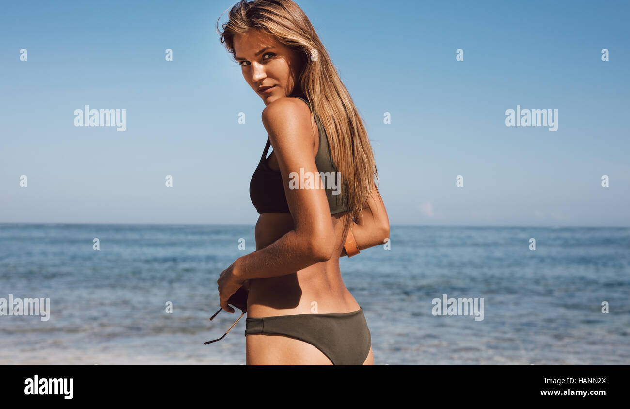 Outdoor shot of beautiful young female model in bikini standing on the beach and looking at camera. Stock Photo