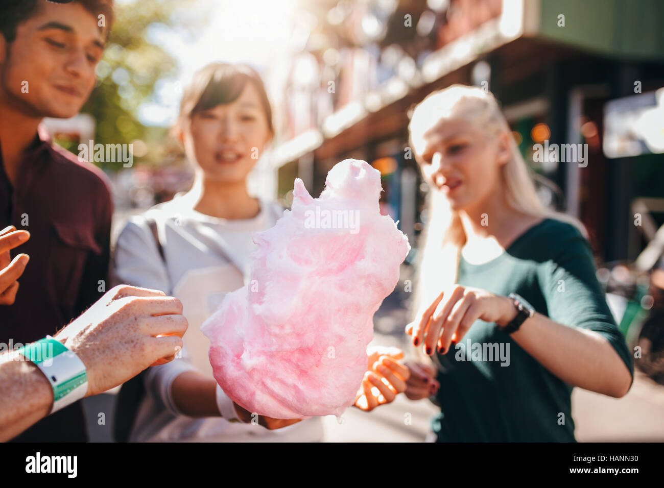 Three young people sharing cotton candyfloss at amusement park. Group of friends eating cotton candy together outdoors. Stock Photo