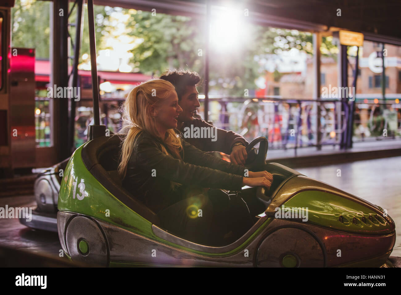 Happy young couple driving a bumper car at amusement park. Young man and woman riding bumper car at fairground. Stock Photo