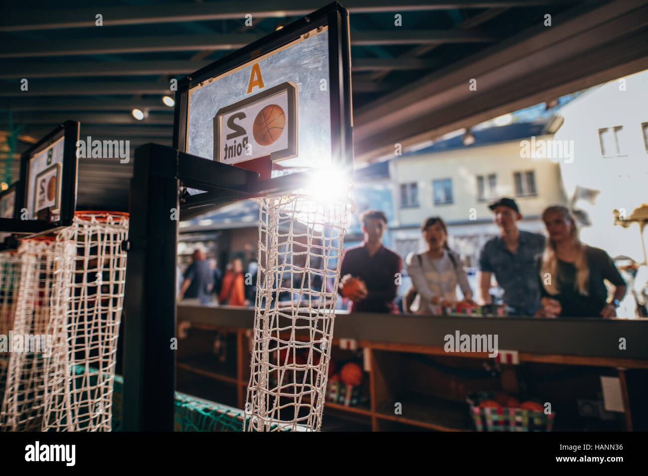 Group of friends shooting hoops at the fair. Focus on basketball hoop at amusement park stall. Stock Photo
