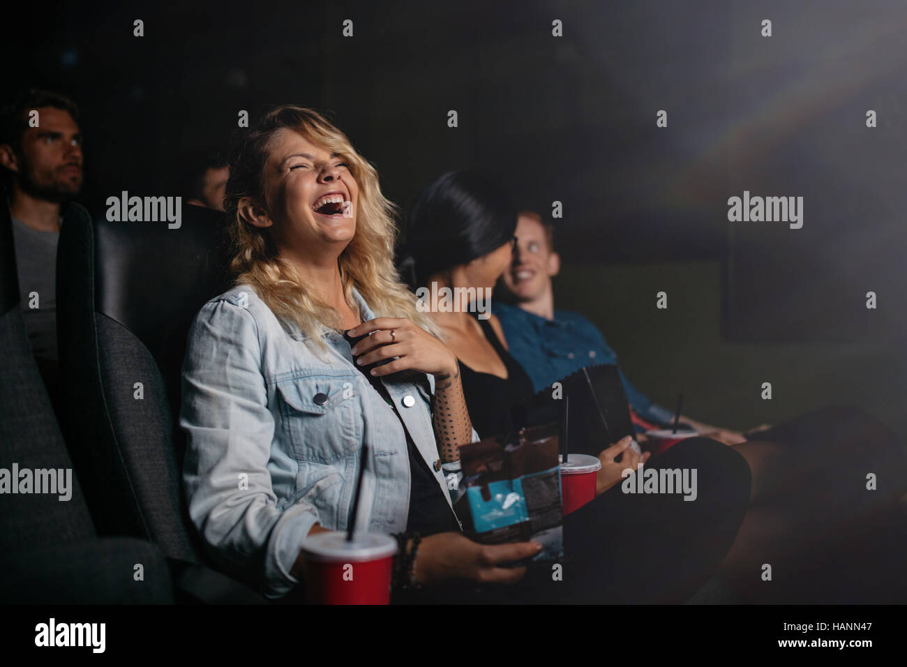 Group of friends sitting in multiplex movie theater and watching comedy movie. Young people watching movie in cinema and laughing. Stock Photo
