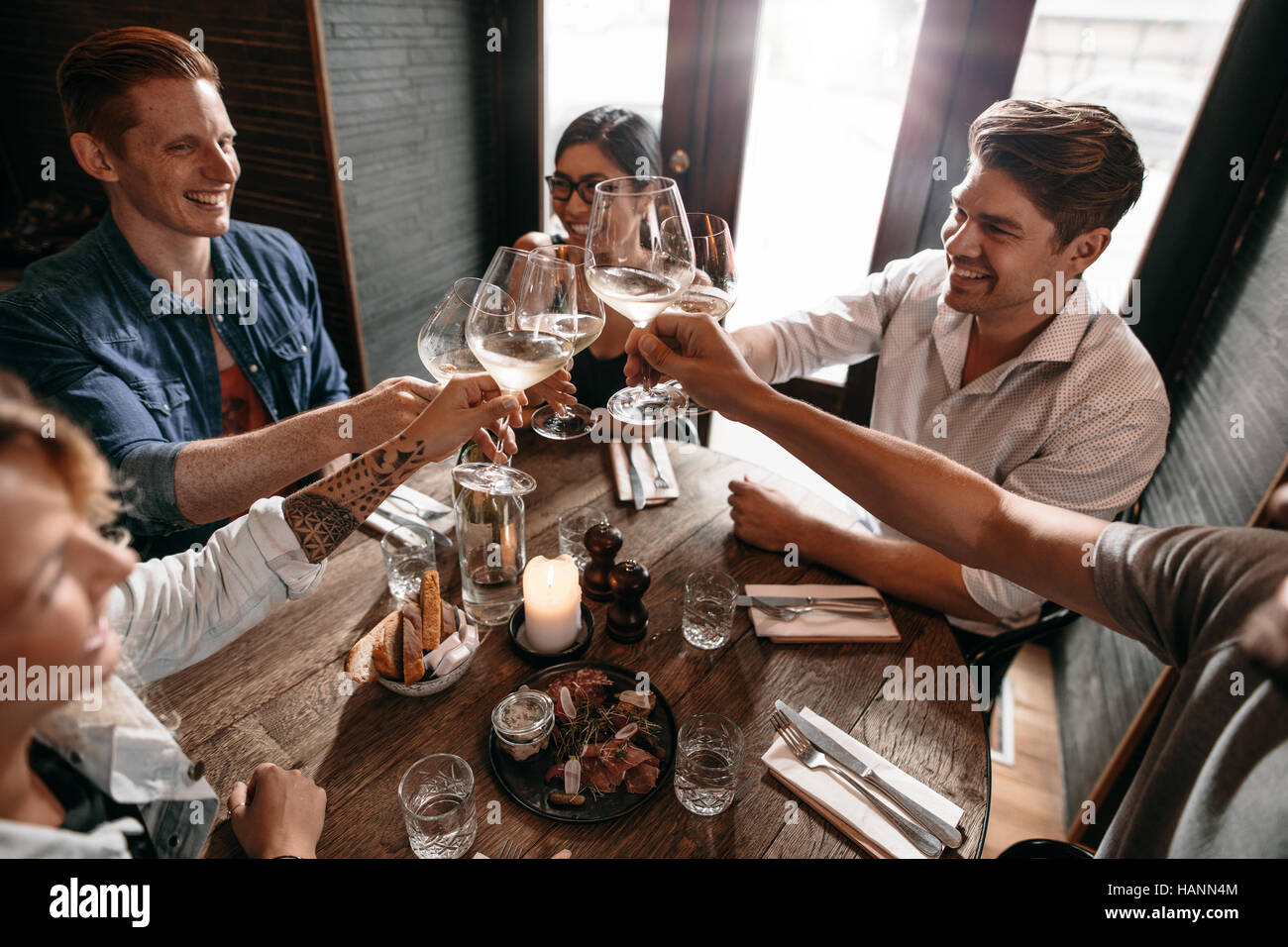 Group of men and women enjoying wine at restaurant. Young friends toasting wine at cafe. Stock Photo