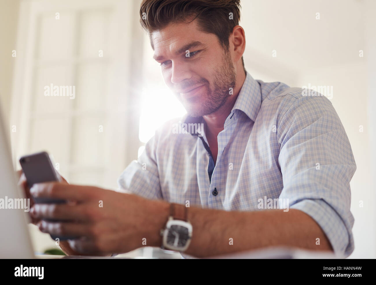 Shot of handsome young man sitting at home using mobile phone. Caucasian business man reading text message on his smart phone. Stock Photo
