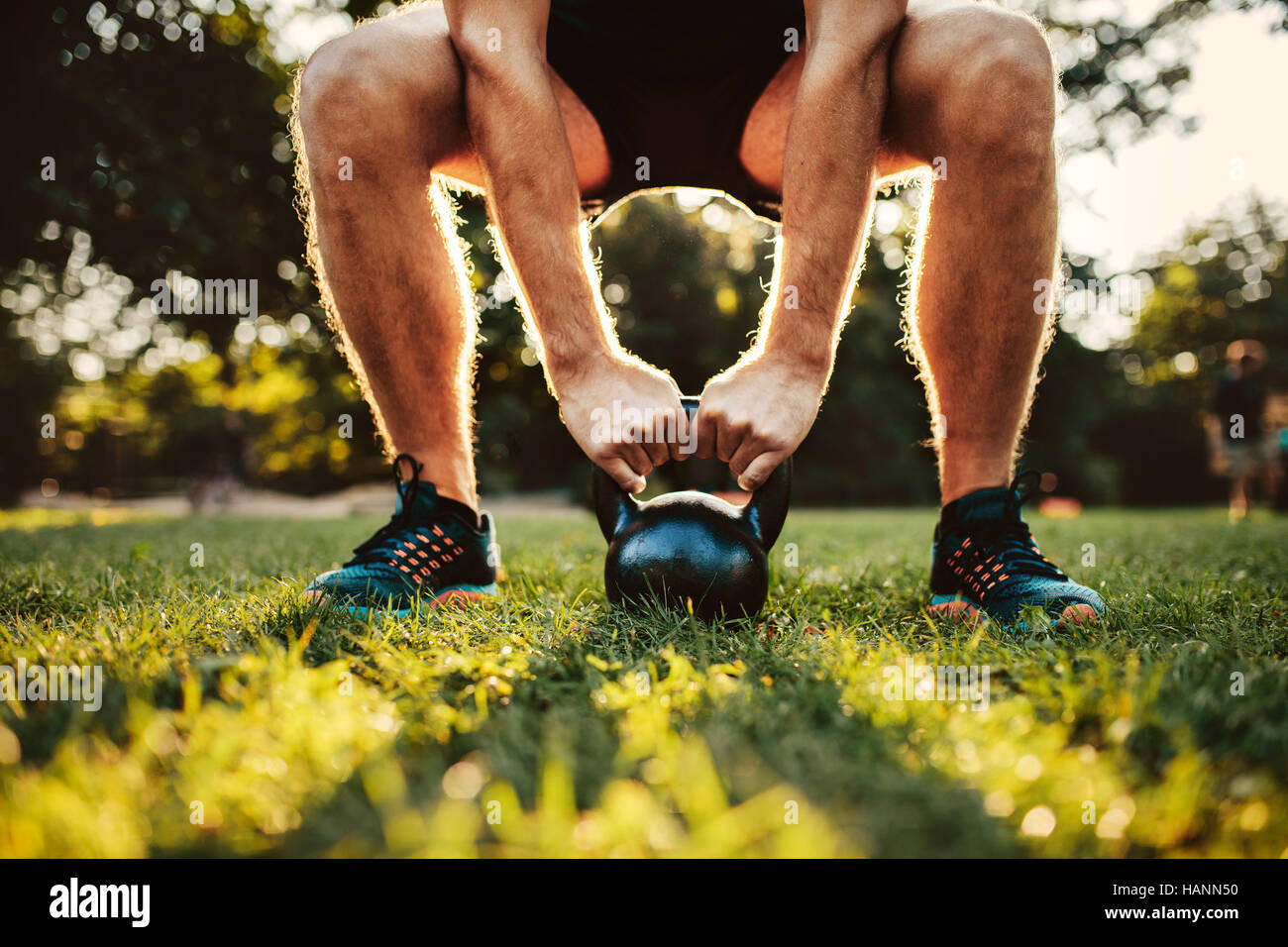 Cropped shot of fit young man doing kettlebell workout in the park, focus on hands holding kettle bell on grass. Stock Photo