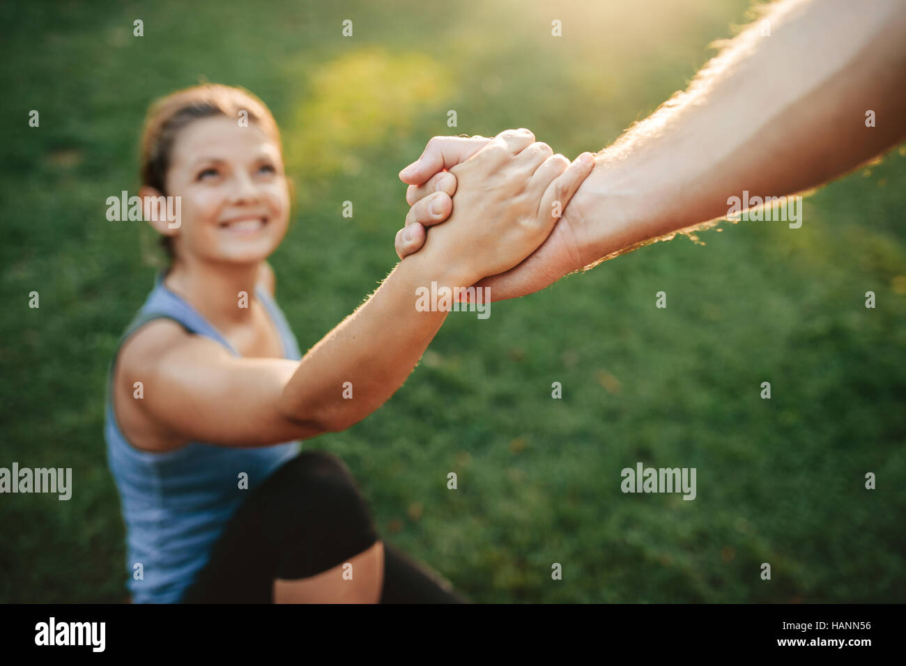 Close up shot of man helping woman to stand up. Focus on hands of couple exercising at park. Stock Photo